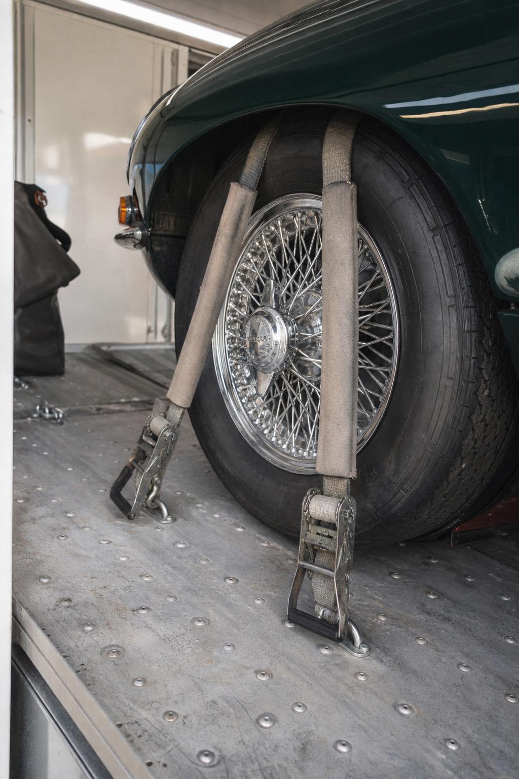 Foam-padded soft-tie straps cradling a chrome wire wheel inside an enclosed trailer